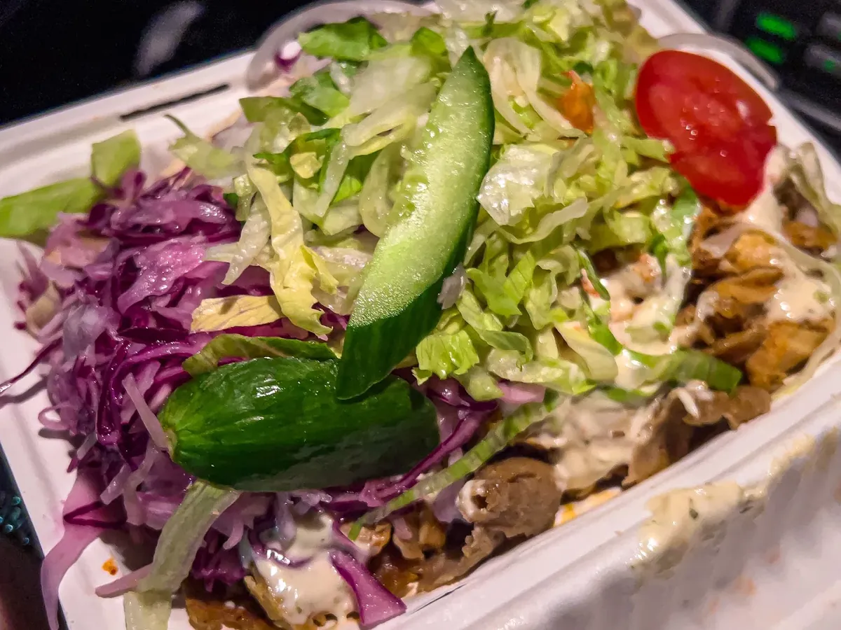Doner meat box topped with shredded lettuce, red cabbage, cucumber, tomato and garlic sauce
